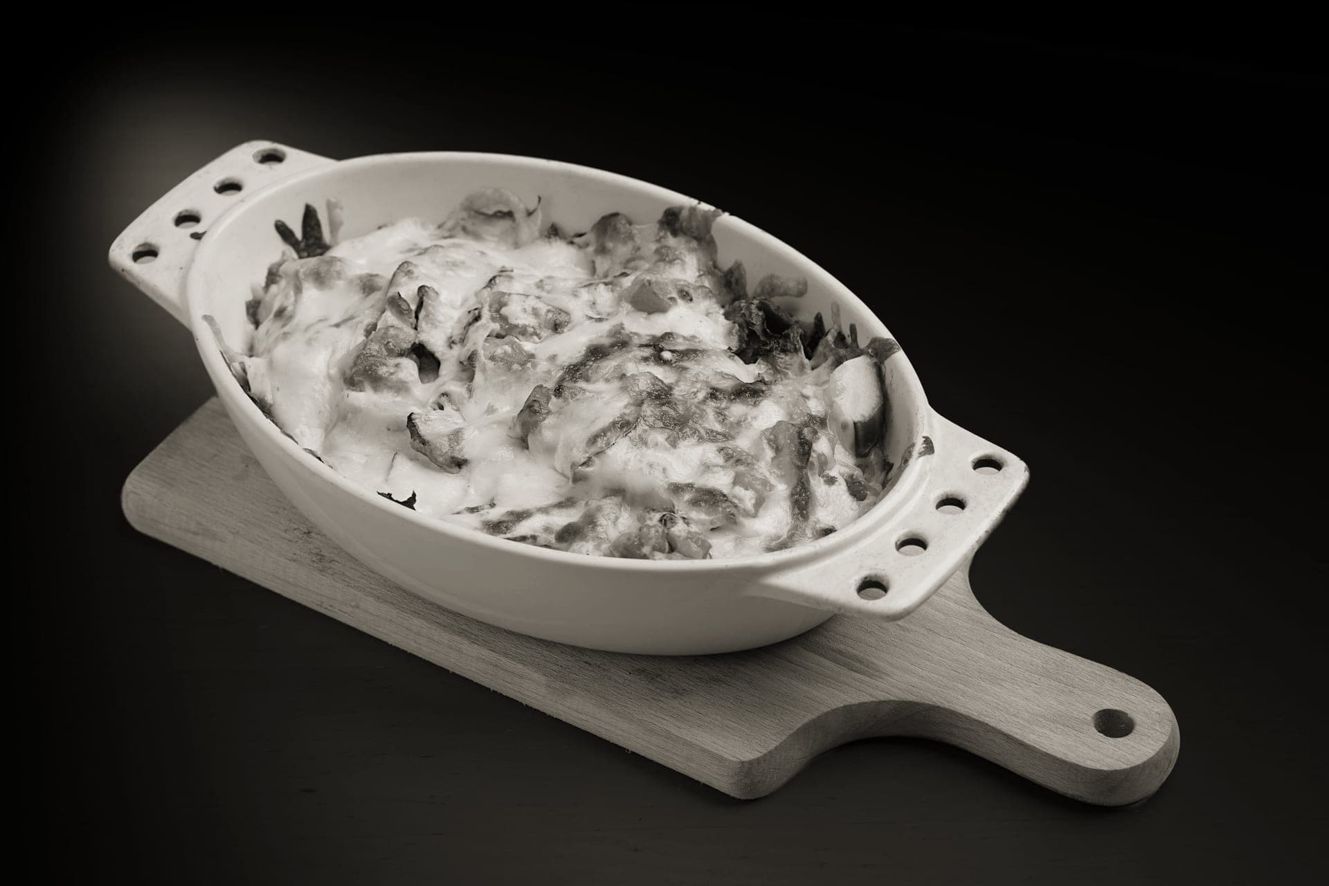 A baked side dish in a white oval casserole dish on a wooden board