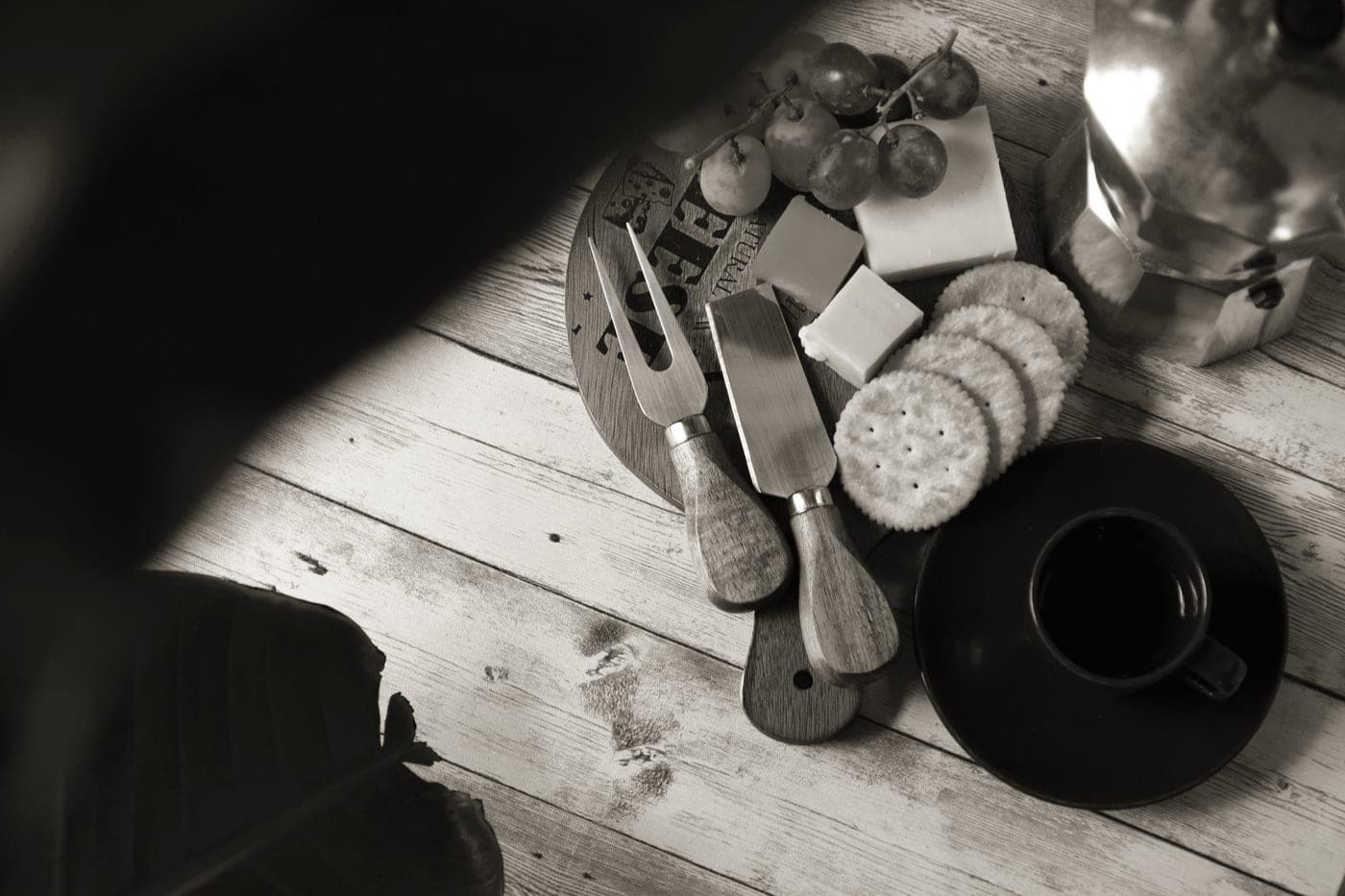 A cheese board with wedges of cheese, crackers and small knives
